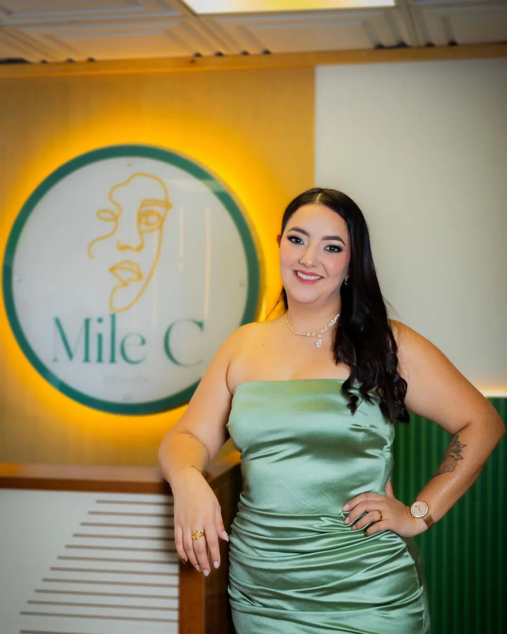 Ana Milena Ceballos, permanent makeup artist, smiling in front of the Mile C Beauty studio sign